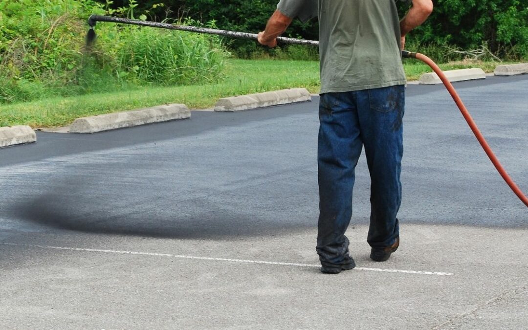 man spraying asphalt-based sealcoat on driveway