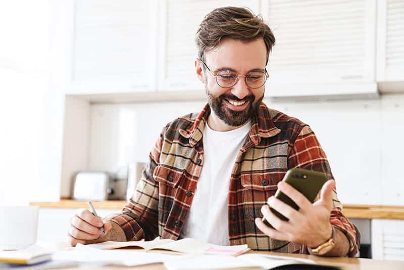 Old man smiling infront of phone whiling taking notes. Happy about the leads that coming in. Old man smiling infront of phone whiling taking notes. Happy about the leads that coming in.