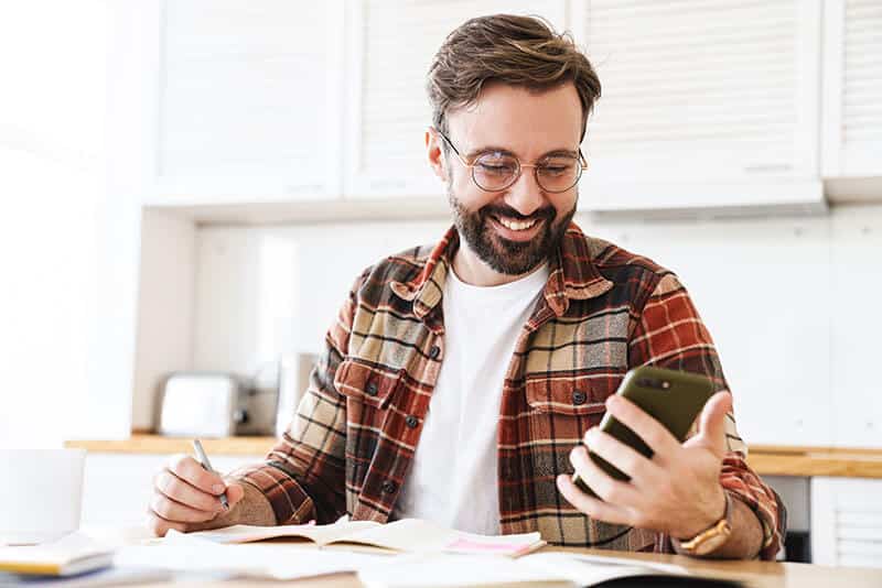 Old man smiling infront of phone whiling taking notes. Happy about the leads that coming in.